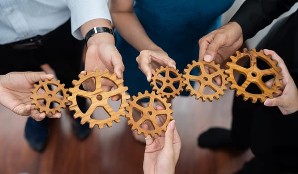 Office worker holding cog wheel as unity and teamwork in corporate workplace concept. Diverse colleague business people showing symbol of visionary system and mechanism for business success. Concord