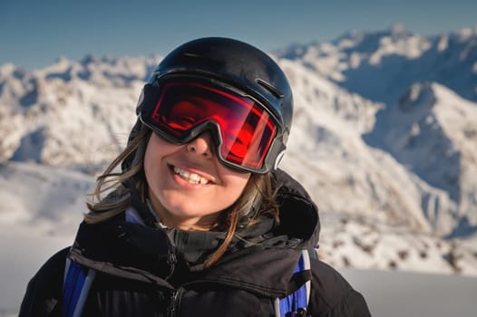 a beautiful girl in a black jacket, snow glasses and a helmet on her head, smiles in the winter mountains on a sunny day. enjoying your holiday at a ski resort