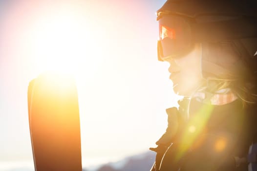 Ski portrait of a woman in a helmet, cool ski goggles on a cold sunny day. A smiling girl in profile stands in the mountains and looks at the beautiful views.