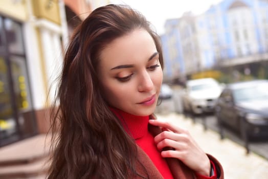 Portrait of a beautiful stylish dreaming lady in a brown autumn coat on the street.