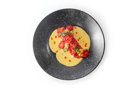 Salmon tartare with strawberries, lots of sauce and chili threads on a black plate isolated