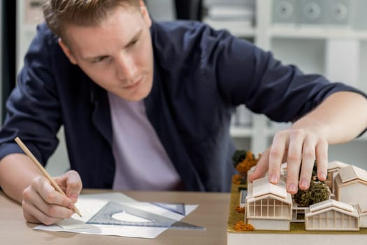 Architect designer studies elegant house model, reviewing structure design for improvement with construction plan on table. Creativity and innovation in architectural design. Iteration