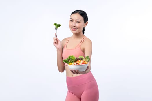 Young sporty Asian woman in sportswear holding salad bowl fill with vibrant of fruit and vegetable. Natural youthful and fit body lifestyle with balance nutrition on isolated background. Vigorous