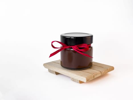 Elegant chocolate spread jar with red ribbon on wooden platform isolated on white background.