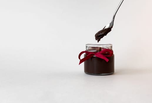 Elegant jar of chocolate spread with ribbon and spoon against minimalist background.