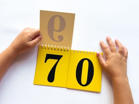 Childs hands flip through yellow pages with numbers. Displaying number 70 on white background.