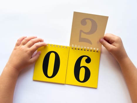 Child flipping calendar pages to change date on desk.