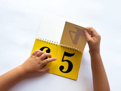 A child turns a page of learning numbers to the next number on a bright yellow background.