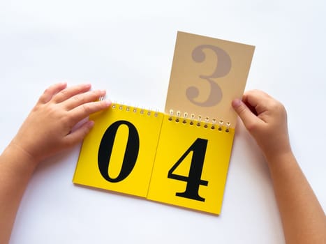 Childs hands turning pages on educational flip calendar with bold numbers.