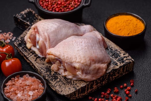 Fresh raw chicken thighs with salt and spices on dark concrete background