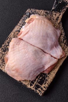 Fresh raw chicken thighs with salt and spices on dark concrete background