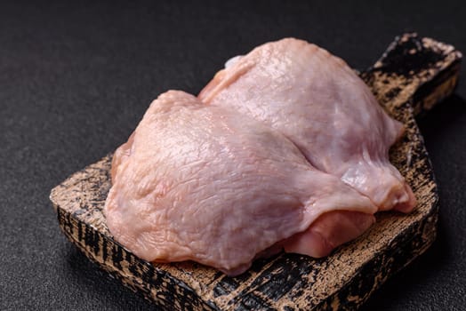 Fresh raw chicken thighs with salt and spices on dark concrete background