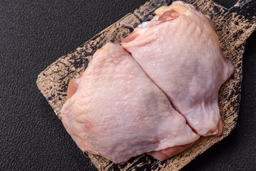 Fresh raw chicken thighs with salt and spices on dark concrete background