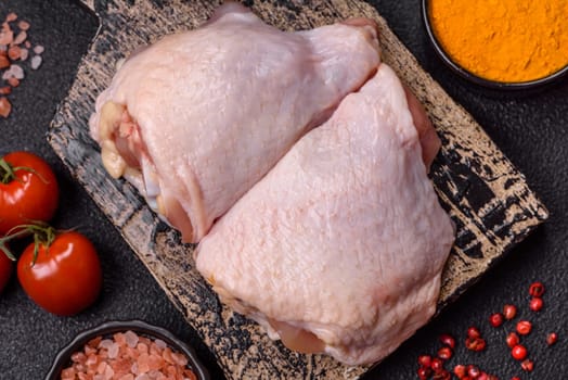 Fresh raw chicken thighs with salt and spices on dark concrete background