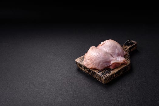 Fresh raw chicken thighs with salt and spices on dark concrete background