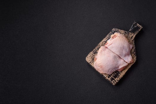 Fresh raw chicken thighs with salt and spices on dark concrete background