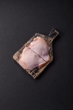 Fresh raw chicken thighs with salt and spices on dark concrete background