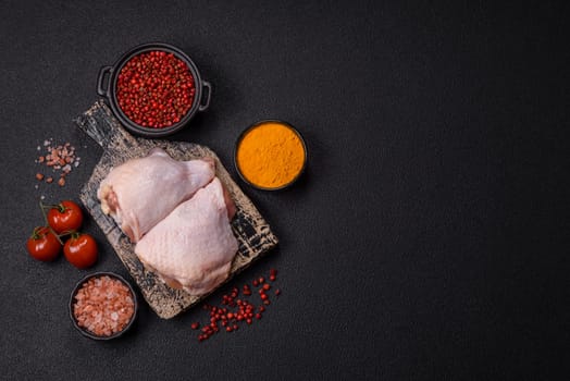 Fresh raw chicken thighs with salt and spices on dark concrete background
