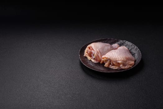 Fresh raw chicken thighs with salt and spices on dark concrete background