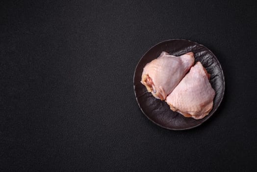 Fresh raw chicken thighs with salt and spices on dark concrete background