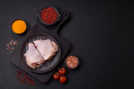 Fresh raw chicken thighs with salt and spices on dark concrete background