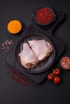 Fresh raw chicken thighs with salt and spices on dark concrete background