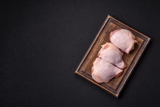 Fresh raw chicken thighs with salt and spices on dark concrete background