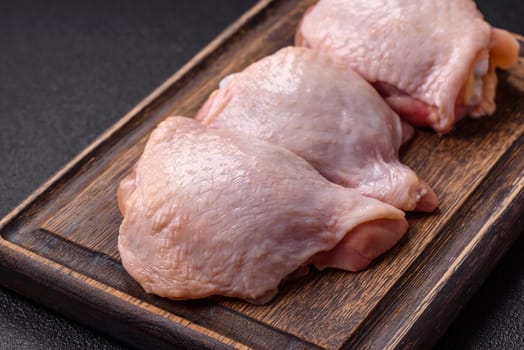 Fresh raw chicken thighs with salt and spices on dark concrete background