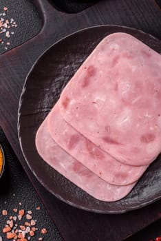 Boiled ham with salt and spices cut into slices on dark concrete background