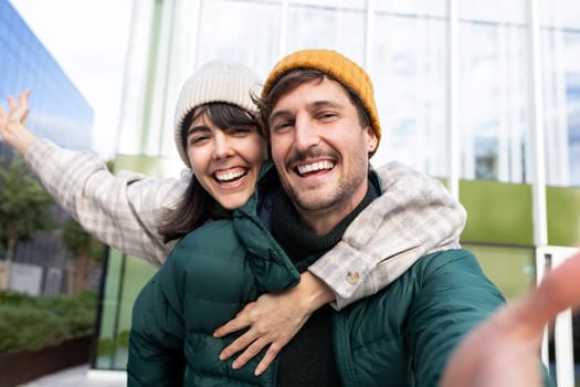 Cheerful man giving piggyback ride to girlfriend while taking selfie in city