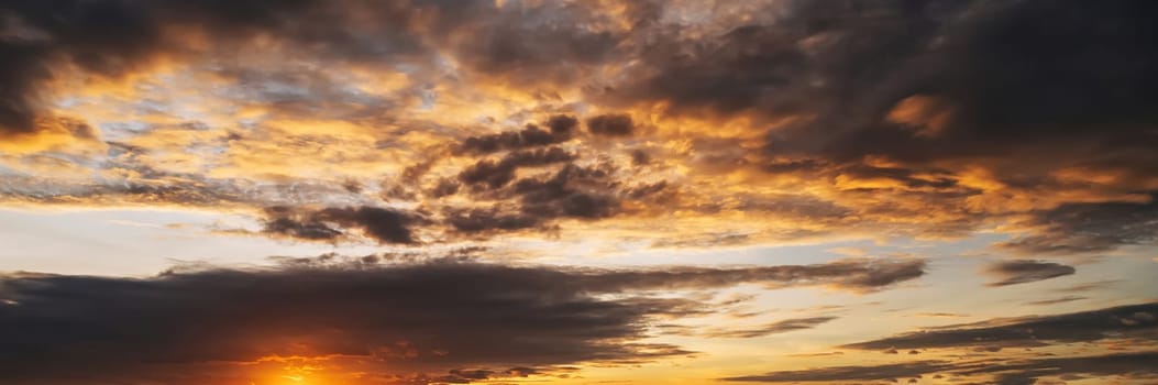 orange sunset in a cloudy sky with clouds at sunset in evening. Panoramic background with sky