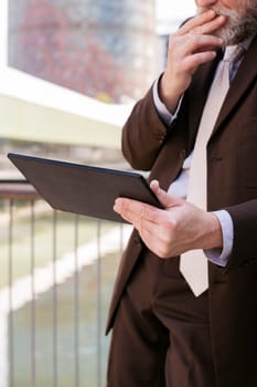 close up of a pensive unrecognizable man in formal outfit browsing tablet while standing at city, concept of technology of communication and business lifestyle