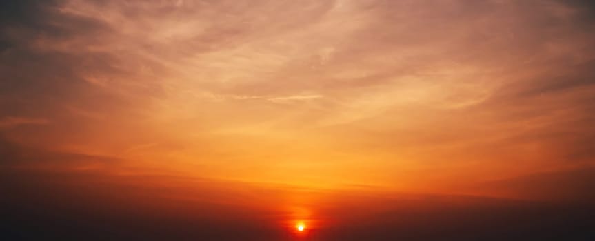 Panorama with an orange sunset and sun in a cloudy sky with clouds. Background with sky at sunrise