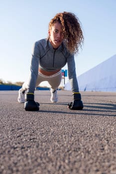 latin sports woman in sportswear doing push ups with boxing gloves on asphalt pavement, concept of urban sport and healthy lifestyle