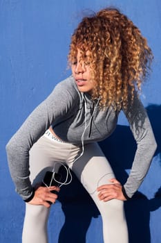sports woman with curly hair resting exhausted during workout while listening music from mobile phone, concept of sport and healthy lifestyle