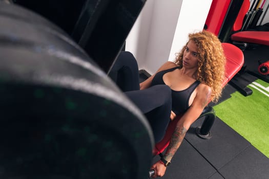 from above hispanic sportswoman with curly hair doing exercises on leg press machine during training at gym, concept of fitness and active lifestyle