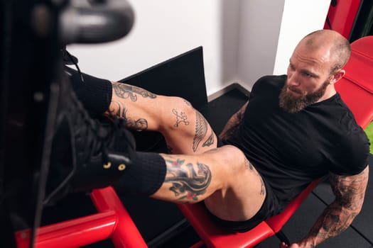 from above of muscular sportsman with tattoos doing exercises on leg press machine during workout in gym, concept of fitness and active lifestyle