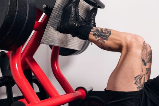 crop of the legs of an unrecognizable muscular sportsman with tattoos doing exercises on leg press machine during workout in gym, concept of fitness and active lifestyle