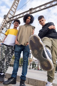 from below of three diverse teenager friends doing kick and looking at camera challenging, concept of youth and urban lifestyle