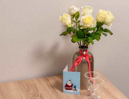 Shot of the white roses in stylish metal vase. Christmas greeting card next to it.