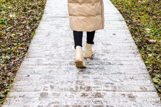 Woman walks on the wooden path walk in the park covered with frost