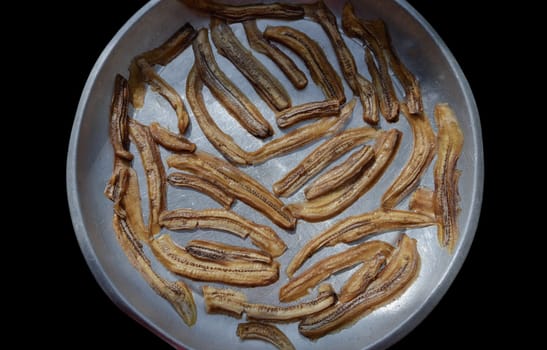 Top view of Natural Dehydrated Bananas on steel round tray with Black background. Delicious sun-dried Sliced Banana, Top view, use it as your Wallpaper, Poster and Space for text, Selective focus.