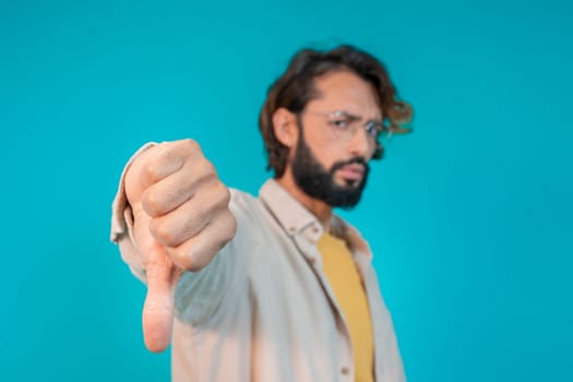 Young man doing thumb down gesture with hand standing over isolated blue background. High quality photo
