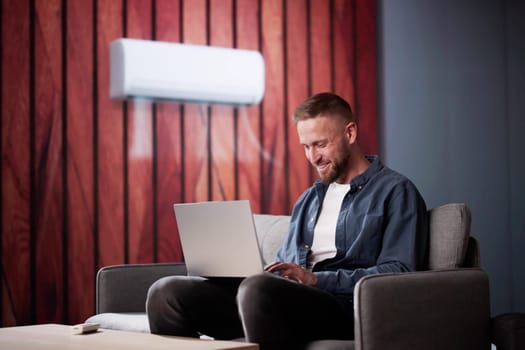 Happy Young Man Holding Remote Control Relaxing Under The Air Conditioner