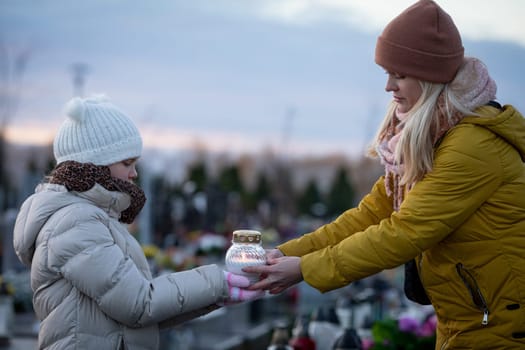 A deeply touching scene depicts a woman and a child holding a glowing lantern at a serene cemetery during sunset