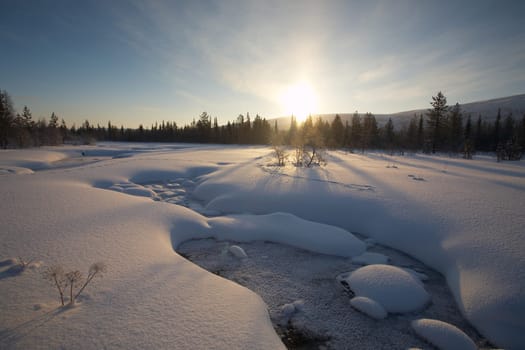 beautiful arctic winter landscape with snowy forest in the background, blue sky and sun setting on the horizon. cold climate