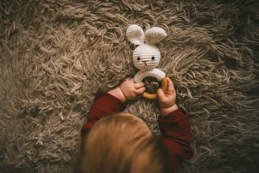 Adorable baby playing with bunny toy on fluffy brown bed coat. Babyhood and playtime concept. High quality photo