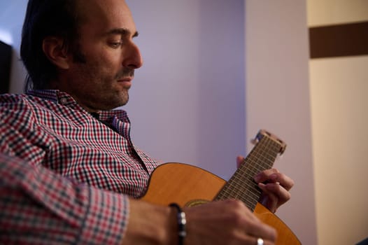 A close-up of a man playing an acoustic guitar indoors, conveying focus and passion. The ambient lighting creates a warm and relaxed atmosphere celebrating the art of music.