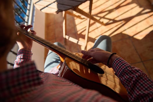 A cozy moment captured from above of a person strumming a guitar while enjoying a sunny day on a tile-floored balcony. The sunlight and relaxed atmosphere suggest leisure and creativity.