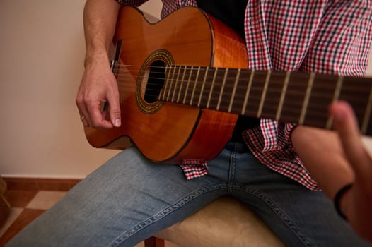 A close-up image of an individual strumming an acoustic guitar while seated, with one hand on the fretboard and the other plucking strings. The scene exudes a casual and musical atmosphere.